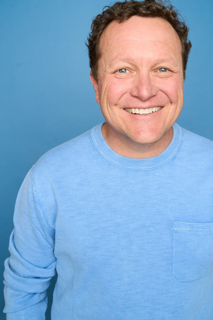 Jay Johnson smiling in a blue sweater